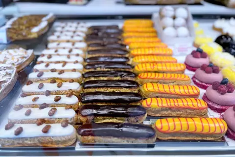 Une alléchante liste pâtisserie française : éclairs au chocolat, à la vanille et au glaçage jaune rayé de rouge, ainsi que des tartelettes aux amandes.