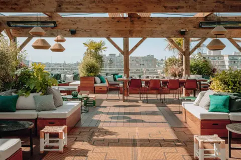Le perchoir Ménilmontant, un rooftop chic avec vue sur Paris. Canapés confortables, tables dressées, végétation luxuriante et ambiance estivale.
