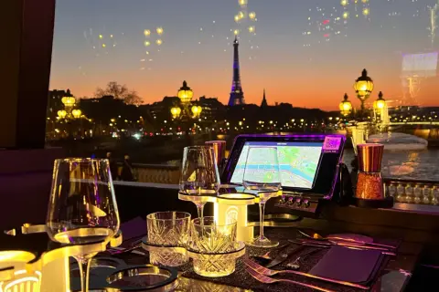 Vue sur Paris au crépuscule, avec la Tour Eiffel illuminée. Une table dressée pour un dîner romantique, parfaite pour savoir où manger après minuit.