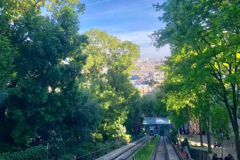 Vue sur le funiculaire de Montmartre, avec Paris en arrière-plan. Les arbres verdoyants encadrent la scène.