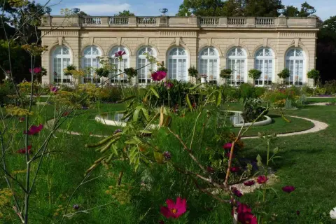 Jardin fleuri devant un bâtiment classique, avec des arches et des fenêtres, au Bois de Boulogne.