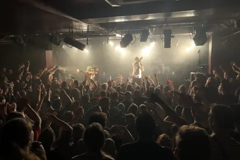 Foule en délire dans une salle de concert, le nombre de places semble limité mais l'ambiance est électrique.