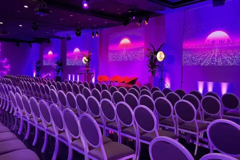 Un auditorium à Paris, baigné de lumières violettes, prêt pour un événement futuriste. Des rangées de chaises attendent les invités.