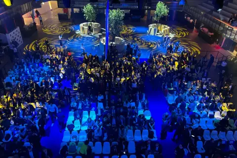 Vue aérienne d'une foule assise dans une **arena Paris** illuminée de bleu, avec des motifs jaunes au sol.