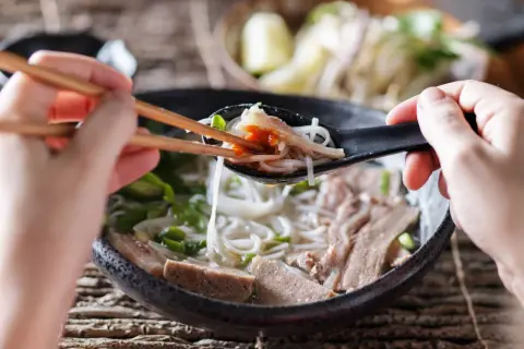 Une cuillère de ce meilleur pho, remplie de nouilles, de viande et d'une touche de sauce piquante, est soulevée avec des baguettes.