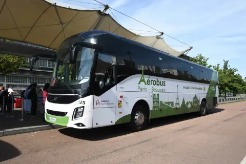 L'Aérobus Paris-Beauvais, un bus blanc et vert orné de monuments parisiens, attend des passagers sous une structure de toit.
