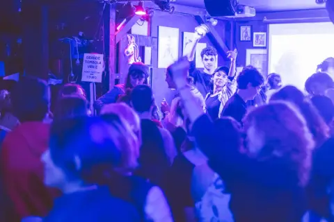 Ambiance festive dans un bar du Marais, une foule profite de la musique sous des lumières bleues et violettes.
