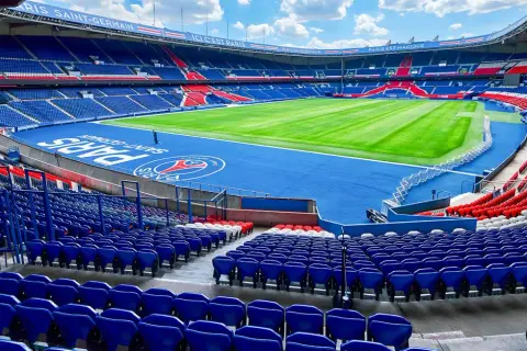 Vue panoramique du **Parc des Princes** vide, avec ses tribunes bleues et rouges, son terrain de football verdoyant et le logo du PSG au centre.