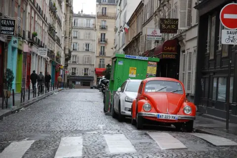 Une rue pavée à Paris, avec une Coccinelle rouge garée. Un panneau "parking gratuit Paris" serait le bienvenu ici.