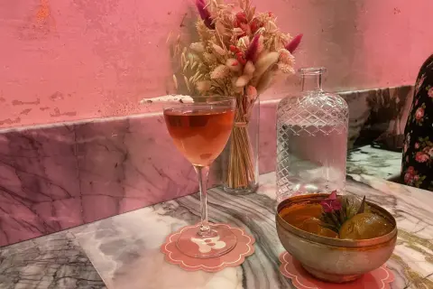 Un cocktail rose et un bol de fruits sur un marbre rose, ambiance douce et romantique d'un bisou bar.