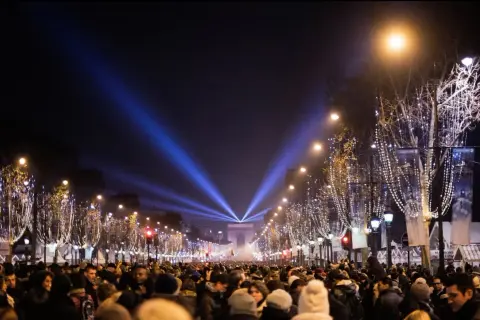 Une foule nombreuse célèbre une **soirée paris** sous les lumières bleues illuminant l'Arc de Triomphe et les arbres décorés de guirlandes.