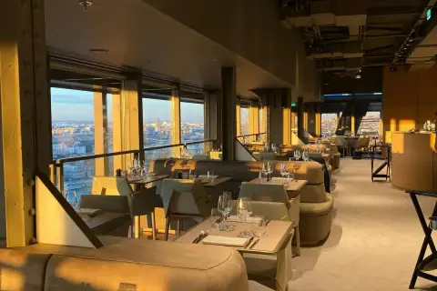 Intérieur d'une brasserie chic avec vue panoramique sur Paris. Les tables sont dressées, prêtes à accueillir les clients pour un dîner inoubliable à la Madame Brasserie Tour Eiffel.