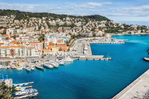 Vue panoramique du port de Nice, avec des yachts amarrés et des bâtiments colorés. On imagine un repas chez Juliette, menu ensoleillé.