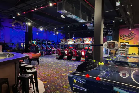 Ambiance de fête foraine à Montparnasse, avec des jeux d'arcade, des tables de air hockey et des murs décorés "Smile world".