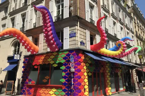 Tentacules colorés géants sortent d'un bâtiment orné de motifs arc-en-ciel, un décor festif pour ce bar gay à Paris.