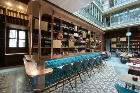 Le bar moderne du "Le Shack Paris" avec son comptoir en cuivre et ses tabourets gris, baigné de lumière naturelle.
