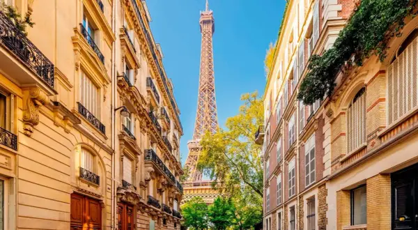 Vue sur la Tour Eiffel entre deux immeubles parisiens, un jour férié de mai. Les balcons ornés et les façades en pierre rappellent le charme de la capitale.