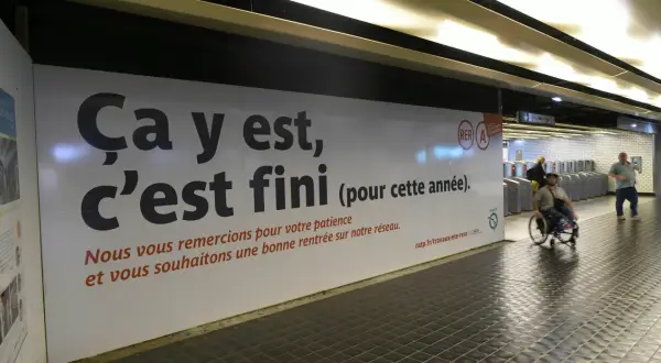 Panneau RATP annonçant la fin des travaux sur le RER A. Une personne en fauteuil roulant passe devant.