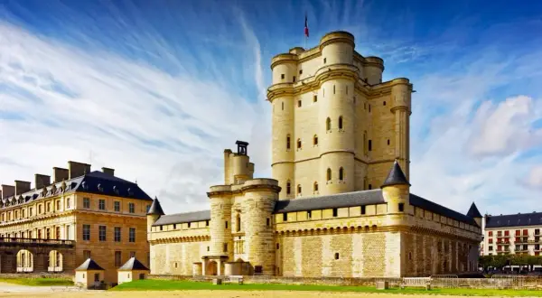 Le majestueux **Château de Vincennes** se dresse sous un ciel bleu éclatant, ses tours imposantes rappelant des siècles d'histoire.