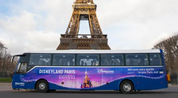 Un bus Disneyland Paris Express, décoré d'un château féerique, passe devant la Tour Eiffel.