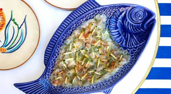 Un délicieux carpaccio de poisson servi dans un plat bleu en forme de poisson, parfait pour un déjeuner à Paris.
