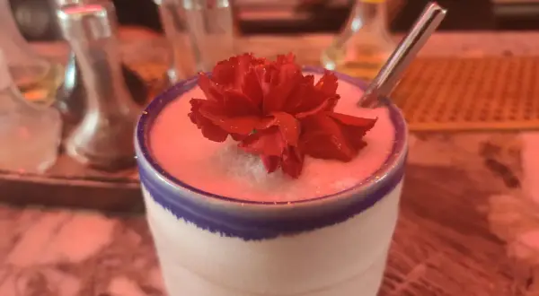 Un cocktail crémeux orné d'une fleur rouge, prêt à être dégusté. Un vrai "menu de bar-bisou" pour une soirée douce.