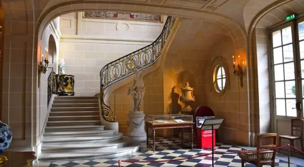 Escalier majestueux du musée Nissim de Camondo, avec sa rampe dorée, sa statue et son sol à damier.