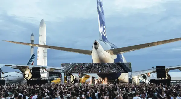 Foule immense devant une scène, sous des avions et des fusées. Ambiance de festival Cercle.