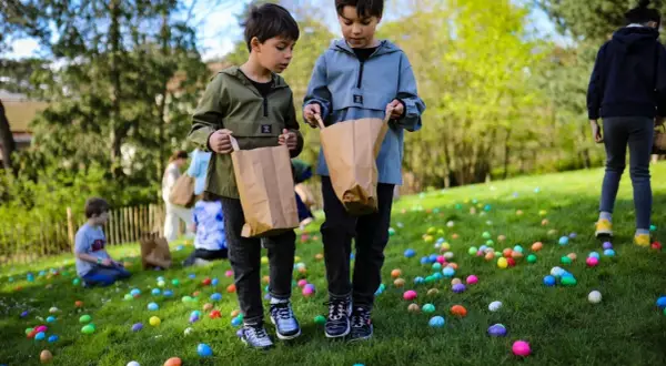 Deux enfants cherchent des œufs colorés dans l'herbe lors d'une chasse aux œufs à Paris.