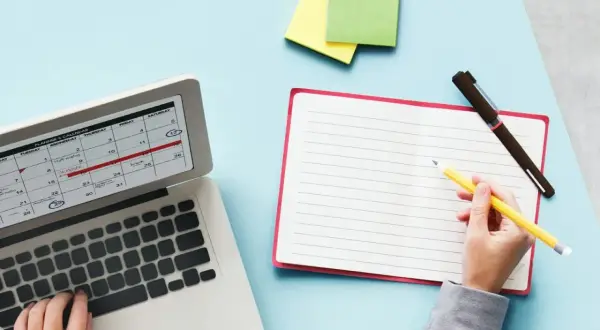 Planification des jours fériés 2026 sur un calendrier d'ordinateur. Une main écrit dans un carnet à côté.