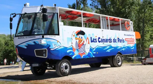 Un bus amphibie décoré de "Les Canards de Paris" avec un canard cartoon, prêt pour une aventure sur l'eau et la terre.