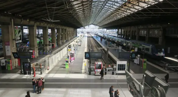 Intérieur lumineux de la gare du Nord, avec des quais, des voies ferrées et des trains. Des voyageurs circulent sous la grande verrière.