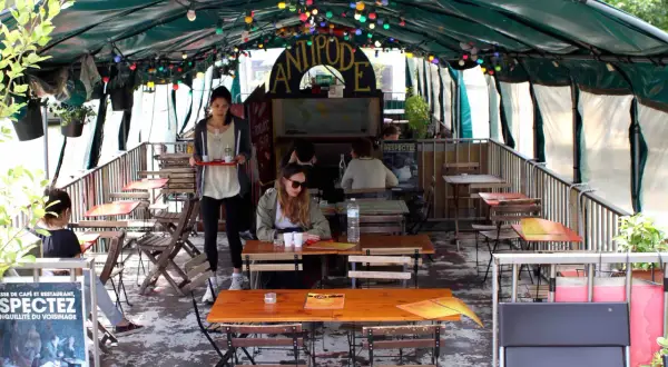 Terrasse animée d'un café-restaurant sur une péniche à Paris, avec des tables en bois, des lumières colorées et des plantes.