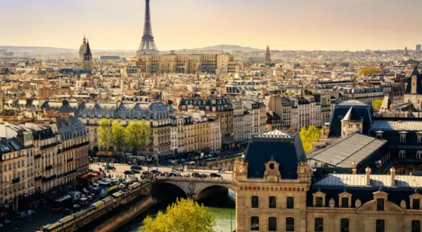 Vue panoramique de Paris en mars, avec la Tour Eiffel dominant un ciel clair. Les toits gris et les bâtiments haussmanniens s'étendent à perte de vue.