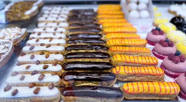 Une alléchante liste pâtisserie française : éclairs au chocolat, à la vanille et au glaçage jaune rayé de rouge, ainsi que des tartelettes aux amandes.