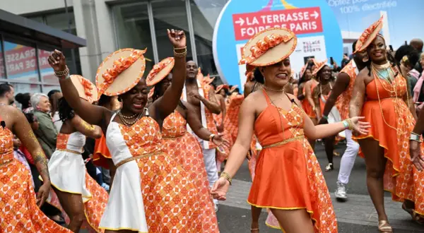 Des danseuses en tenues orange et blanches, chapeaux assortis, célèbrent la foire de Paris 2026 dans une ambiance festive.