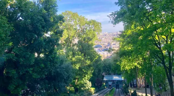 Vue sur le funiculaire de Montmartre, avec Paris en arrière-plan. Les arbres verdoyants encadrent la scène.