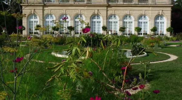 Jardin fleuri devant un bâtiment classique, avec des arches et des fenêtres, au Bois de Boulogne.