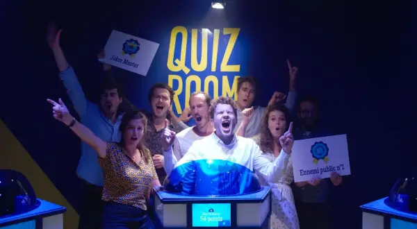 Équipe joyeuse dans une "Quiz Room" à Paris La Villette, célébrant une victoire. Ils tiennent des pancartes "Joker Master" et "Ennemi public n°1".