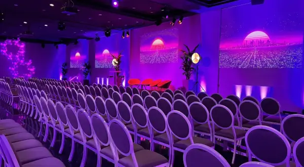 Un auditorium à Paris, baigné de lumières violettes, prêt pour un événement futuriste. Des rangées de chaises attendent les invités.