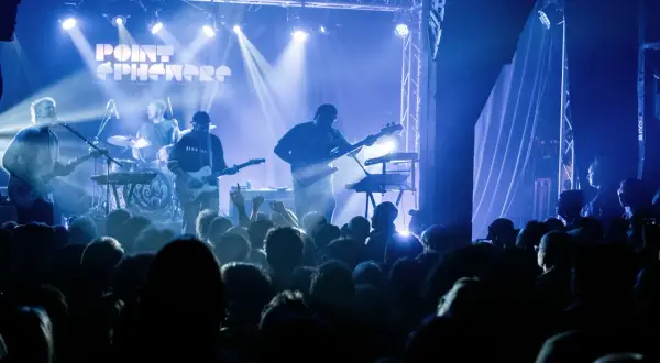 Un groupe joue sur scène sous des lumières bleues. Découvrez les **upcoming concerts in Paris** !