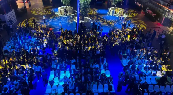 Vue aérienne d'une foule assise dans une **arena Paris** illuminée de bleu, avec des motifs jaunes au sol.