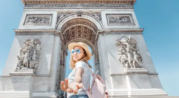 Une jeune femme tend la main devant l'Arc de Triomphe. L'accès au monument est gratuit, une belle opportunité de visite.