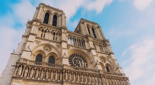 Notre Dame de Paris, une visite inoubliable. La façade majestueuse de la cathédrale se dresse sous un ciel bleu et nuageux.