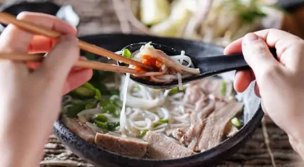 Une cuillère de ce meilleur pho, remplie de nouilles, de viande et d'une touche de sauce piquante, est soulevée avec des baguettes.