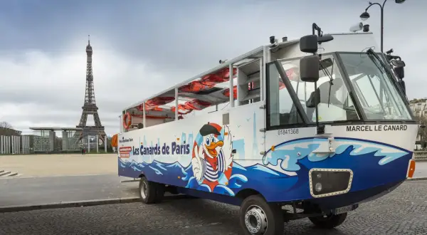 Un bus amphibie "Les Canards de Paris" prêt pour un tour hop on hop off, avec la Tour Eiffel en arrière-plan.