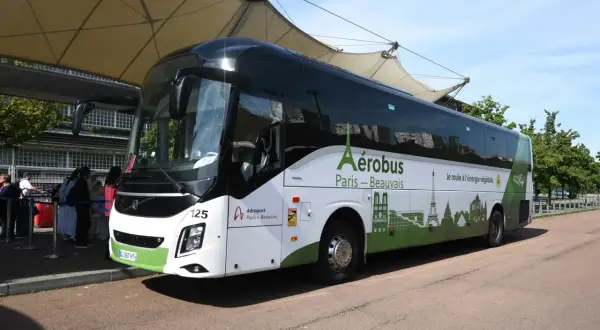 L'Aérobus Paris-Beauvais, un bus blanc et vert orné de monuments parisiens, attend des passagers sous une structure de toit.