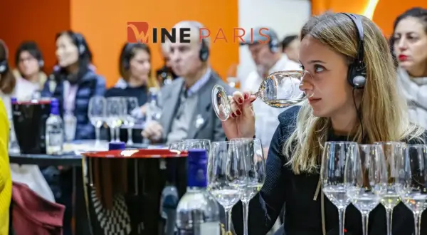 Dégustation de vin à Wine Paris 2026. Une femme hume un verre, casque sur les oreilles, entourée d'autres participants.
