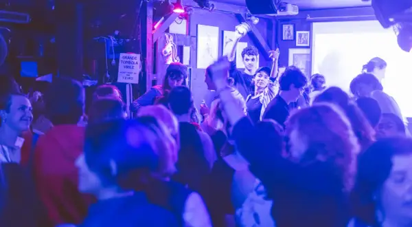Ambiance festive dans un bar du Marais, une foule profite de la musique sous des lumières bleues et violettes.