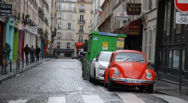Une rue pavée à Paris, avec une Coccinelle rouge garée. Un panneau "parking gratuit Paris" serait le bienvenu ici.